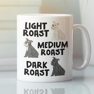 May include: White ceramic coffee mug with a black graphic of three schnauzers of different colors. The text "Light Roast", "Medium Roast", and "Dark Roast" is printed on the mug.