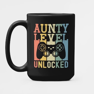 May include: Black coffee mug with a retro-style design featuring a video game controller and the text "AUNTY LEVEL UNLOCKED".