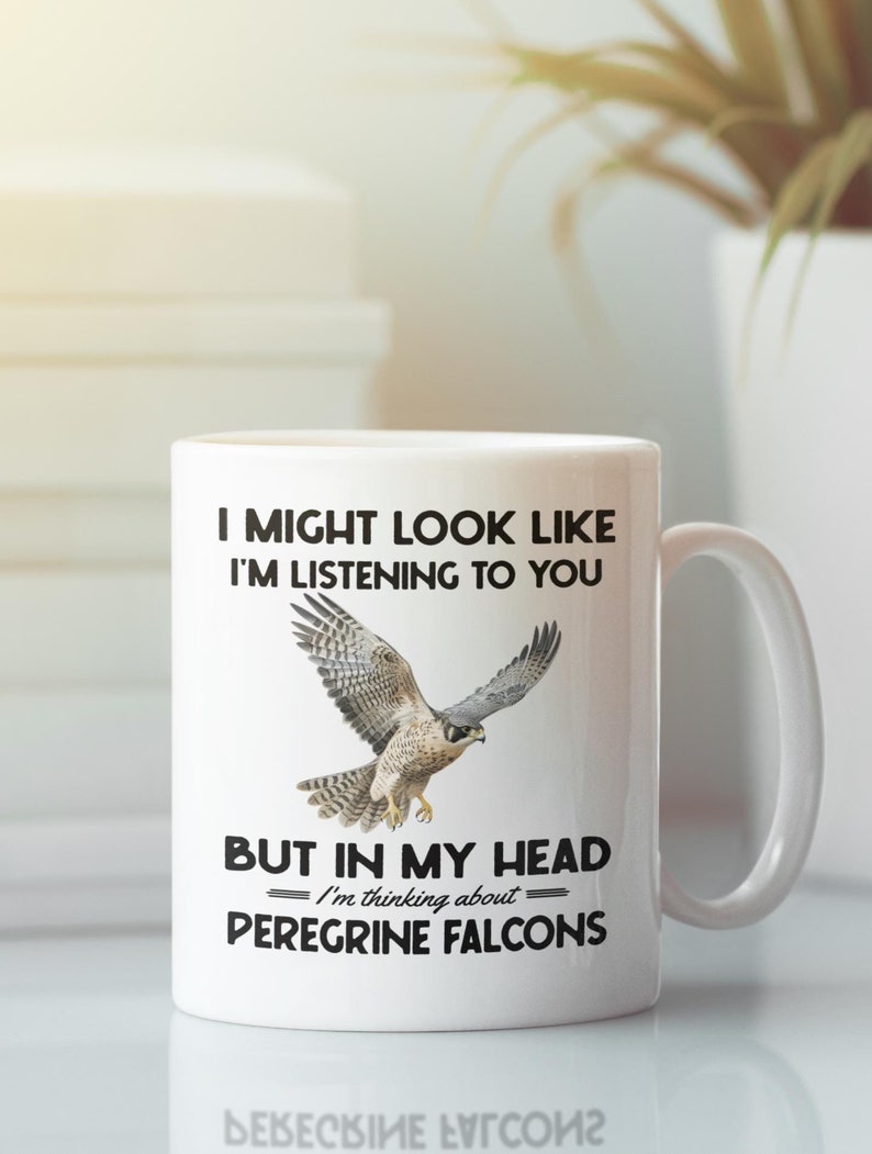 May include: White ceramic coffee mug with a black graphic of a peregrine falcon in flight. The text reads "I might look like I'm listening to you, but in my head I'm thinking about Peregrine Falcons."
