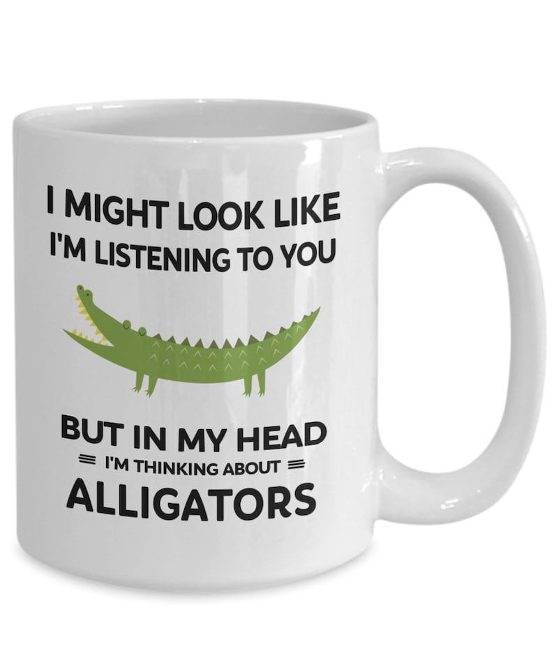 K&ouml;nnte beinhalten: Eine wei&szlig;e Keramik-Kaffeetasse mit einem schwarzen und gr&uuml;nen Alligator-Motiv und dem Text "Ich sehe vielleicht aus, als w&uuml;rde ich zuh&ouml;ren, aber in meinem Kopf = denke ich an = Alligatoren."
