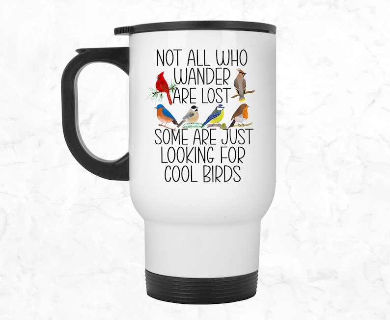 May include: White travel mug with a black handle and black bottom. The mug has a black and white graphic of birds with the text "Not all who wander are lost. Some are just looking for cool birds."