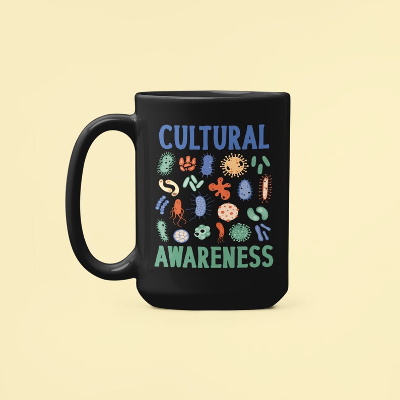 May include: Black ceramic coffee mug with a white handle. The mug features a blue and white graphic that says "CULTURAL AWARENESS" and a variety of colourful bacteria and microbes.