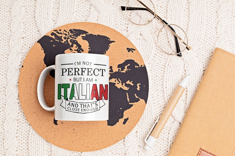 May include: White ceramic mug with the text "I'm not perfect but I am Italian and that's close enough" in black text with a red, white, and green Italian flag design. The mug is sitting on a cork coaster with a black world map design.