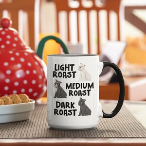 May include: White ceramic mug with a black handle. The mug has a graphic of three miniature schnauzers with the text "Light Roast", "Medium Roast", and "Dark Roast" underneath each dog.