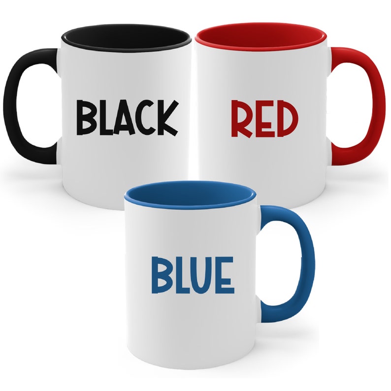 May include: Three white ceramic mugs with colored interiors and handles. One mug has a black interior and handle with the word "BLACK" in black. Another has a red interior and handle with "RED" in red. The third has a blue interior and handle with "BLUE" in blue.