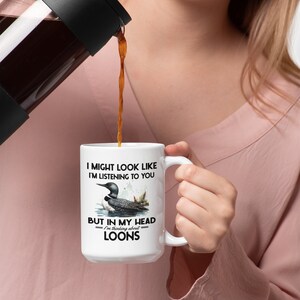 May include: White ceramic coffee mug with a black handle. The mug features a loon bird design with the text "I might look like I'm listening to you, but in my head I'm thinking about loons."