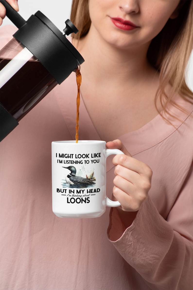 May include: White ceramic coffee mug with a black handle. The mug features a loon bird design with the text "I might look like I'm listening to you, but in my head I'm thinking about loons."