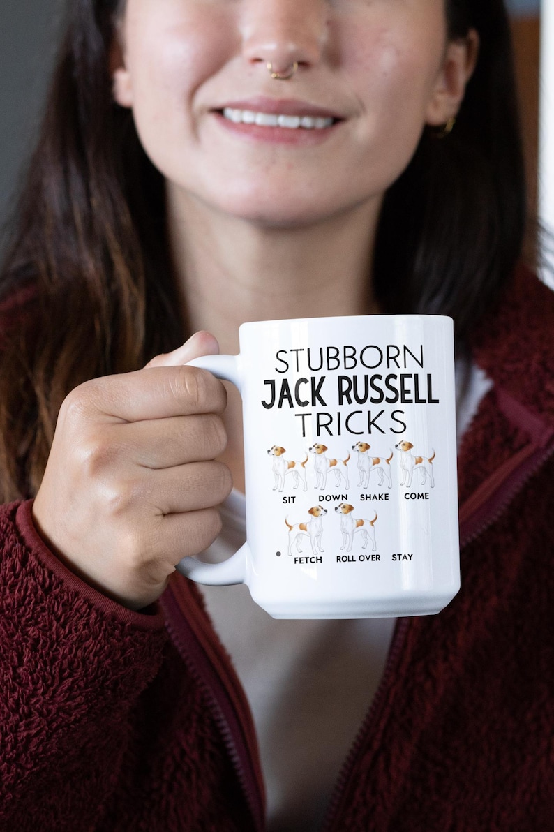 May include: White ceramic mug with the text "Stubborn Jack Russell Tricks" and illustrations of Jack Russell Terriers performing tricks. The tricks include sit, down, shake, come, fetch, roll over, and stay.