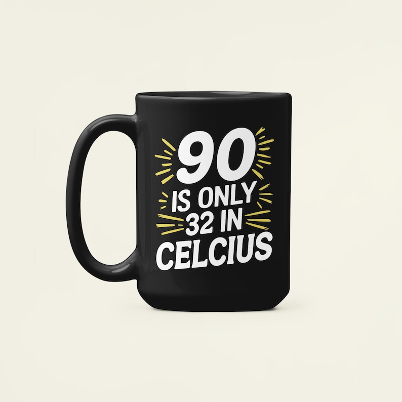 May include: Black ceramic mug with a white and yellow graphic that reads "90 IS ONLY 32 IN CELCIUS". The mug has a large handle and a cylindrical shape. The text is centered on the mug.