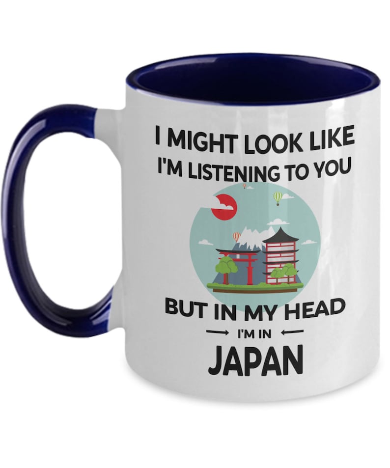 May include: White ceramic coffee mug with a blue rim and handle. The mug features a graphic of a Japanese landscape with a red temple and the text "I might look like I'm listening to you but in my head I'm in Japan."