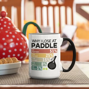 May include: White ceramic mug with a black handle. The mug has a graphic that says "Why I Lose at Paddle" with a list of reasons and percentages. The reasons are: My Partner 51%, The Racket 25%, The Court 15%, The Ball 8%, My Fault 1%.