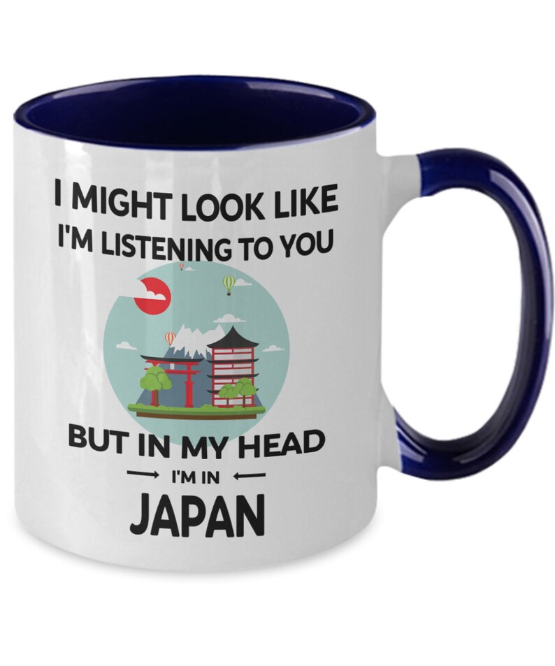 May include: White ceramic coffee mug with a blue rim and handle. The mug features a graphic of a Japanese cityscape with the text "I might look like I'm listening to you, but in my head I'm in Japan."