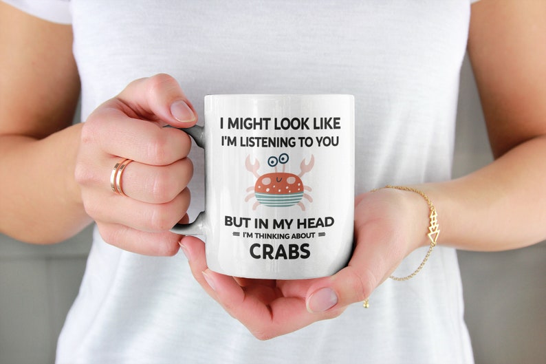 Pu&ograve; includere: Una tazza in ceramica bianca con un'illustrazione di granchio di cartone animato nero e rosso. La tazza recita "Potrei sembrare che ti stia ascoltando, ma nella mia testa sto pensando ai granchi."
