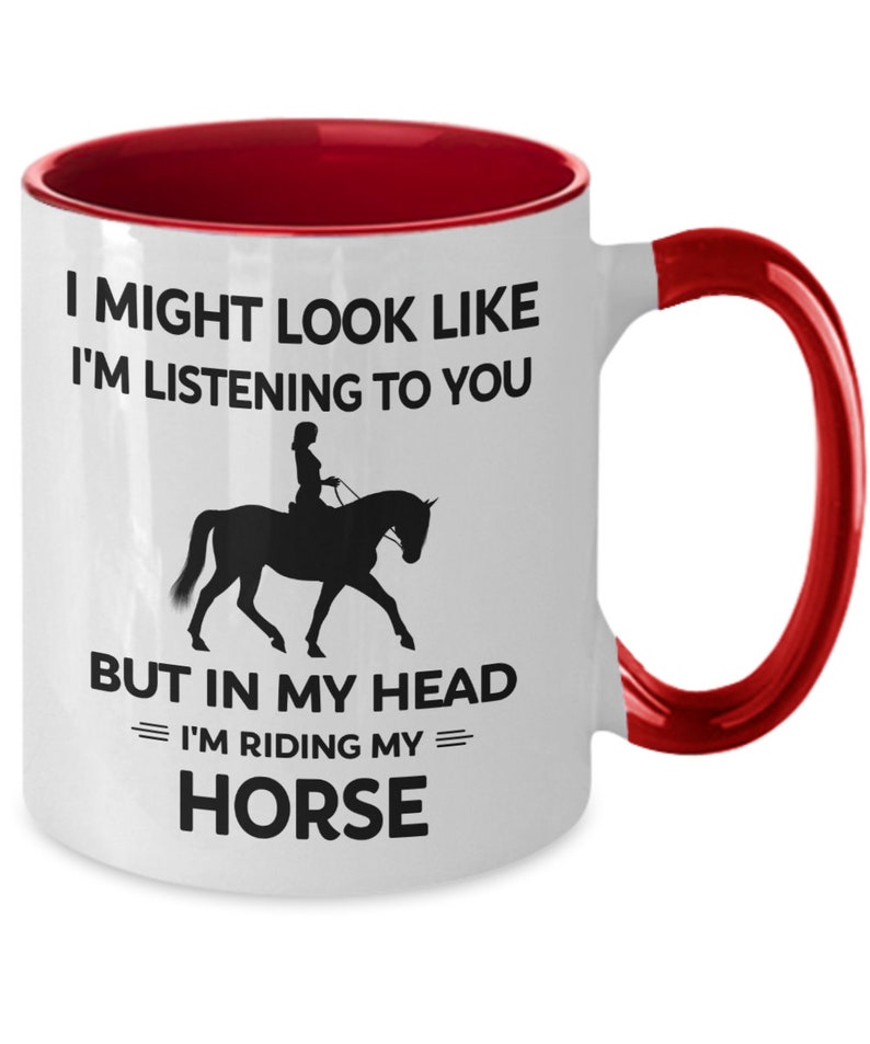 May include: White ceramic coffee mug with a red rim and handle. The mug features a black silhouette of a person riding a horse with the text "I might look like I'm listening to you, but in my head I'm riding my horse."