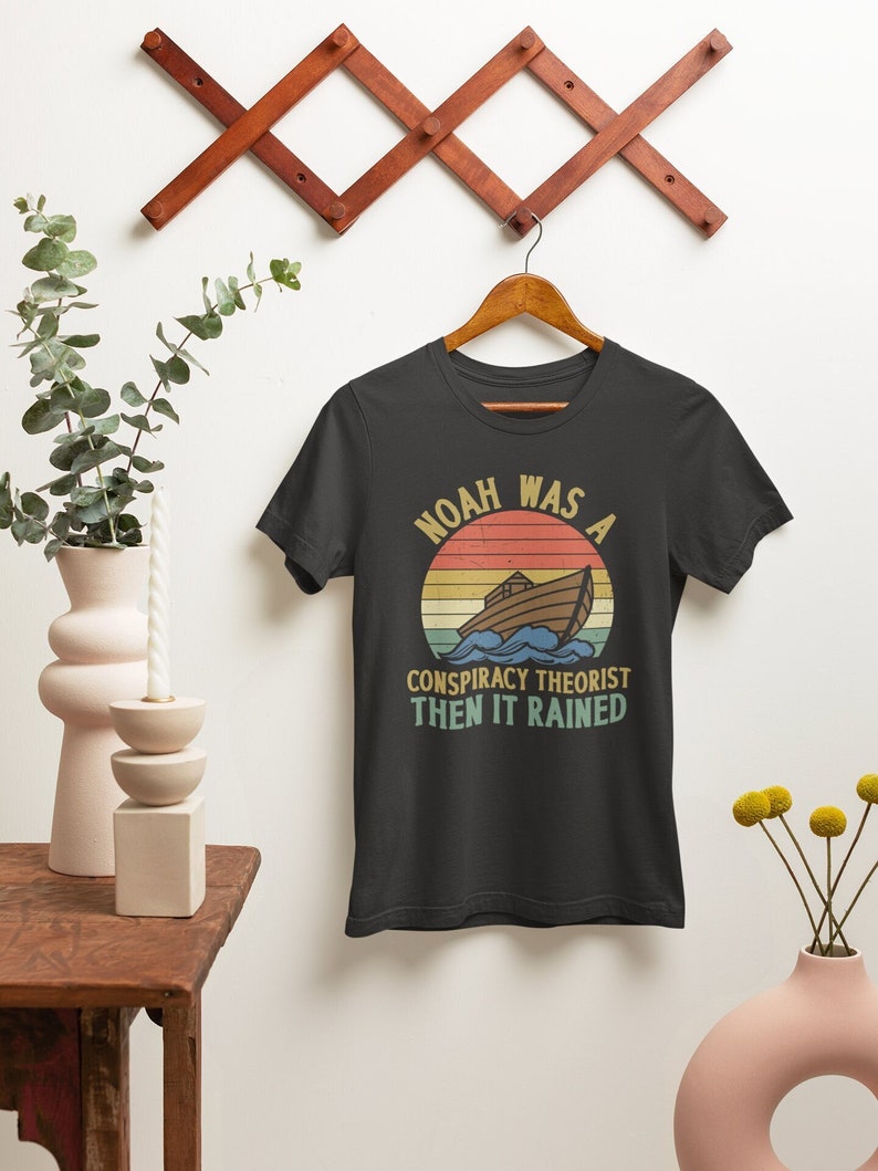 May include: Black t-shirt with a vintage-style graphic of a boat on a sunset with the text "Noah was a conspiracy theorist then it rained".
