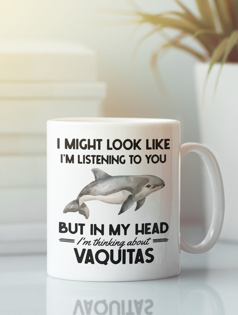 May include: White ceramic mug with a black and white graphic of a dolphin and the text "I might look like I'm listening to you but in my head I'm thinking about VAQUITAS".
