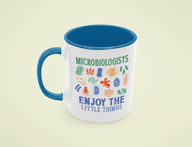 May include: White ceramic mug with a blue rim and handle. The mug has a design of colorful microbes and the text "Microbiologists Enjoy the Little Things".