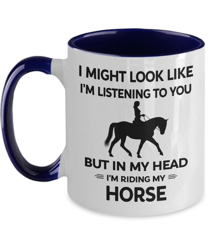 May include: White ceramic coffee mug with a blue rim and handle. The mug features a black silhouette of a person riding a horse with the text "I might look like I'm listening to you but in my head I'm riding my horse."