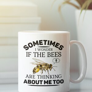 K&ouml;nnte beinhalten: Wei&szlig;e Keramiktasse mit einer schwarzen Grafik, auf der steht "Manchmal frage ich mich, ob die Bienen auch an mich denken". Eine Cartoon-Biene ist abgebildet mit einer Gedankenblase dar&uuml;ber, die eine Strichm&auml;nnchen zeigt.