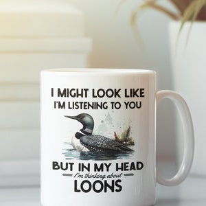May include: White ceramic coffee mug featuring a black loon illustration and the text "I might look like I'm listening to you, but in my head I'm thinking about loons."
