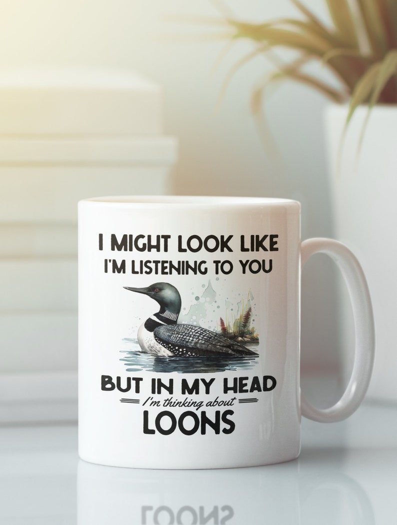 May include: White ceramic coffee mug featuring a black loon illustration and the text "I might look like I'm listening to you, but in my head I'm thinking about loons."