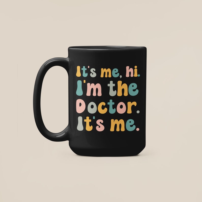 May include: Black coffee mug with the text "It's me, hi. I'm the doctor. It's me." in colorful, playful lettering.