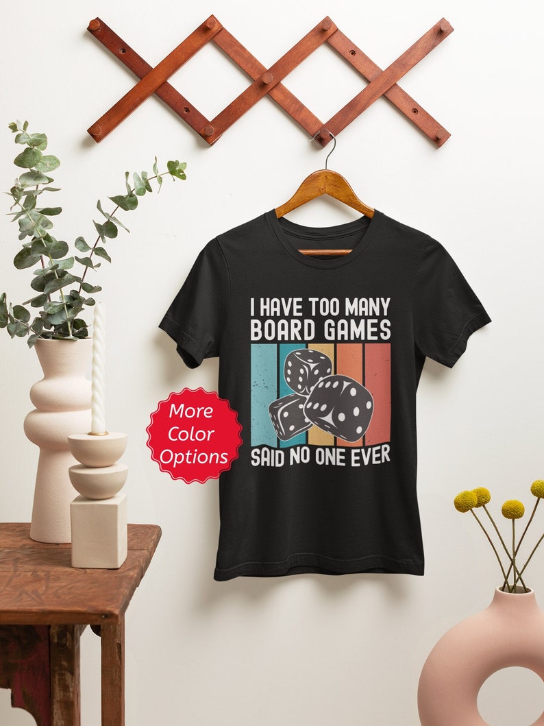 Puede incluir: Camiseta negra con un gr&aacute;fico de estilo vintage que dice "Tengo demasiados juegos de mesa, nadie ha dicho nunca eso". El gr&aacute;fico presenta una pila de dados con un fondo de arco&iacute;ris.