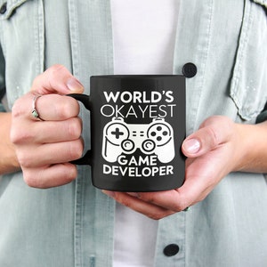May include: Black coffee mug with a white design that says "World's Okayest Game Developer" and a white video game controller graphic.