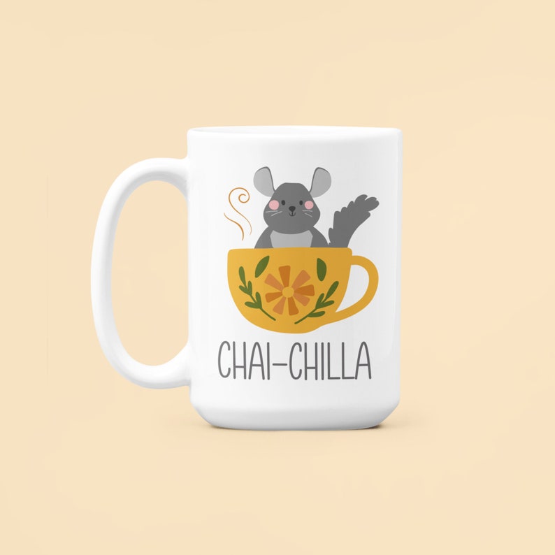May include: White ceramic mug featuring a grey chinchilla sitting in a yellow teacup with a floral design. The text "Chai-Chilla" is printed on the mug.