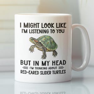 May include: White ceramic coffee mug featuring a black and green illustration of a red-eared slider turtle. The mug reads "I might look like I'm listening to you, but in my head I'm thinking about red-eared slider turtles."
