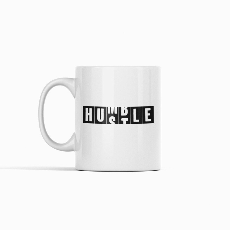 Peut inclure: Une tasse en c&eacute;ramique blanche avec un motif noir qui dit "HUSTLE" dans une police de caract&egrave;res en blocs.