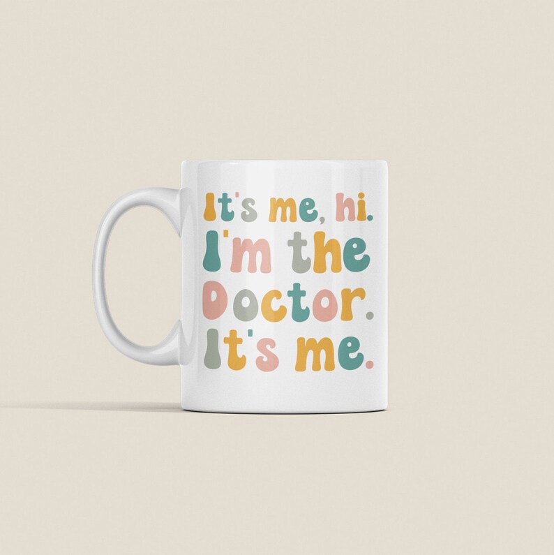 May include: White ceramic mug with a colorful text design that reads "It's me, hi. I'm the doctor. It's me."