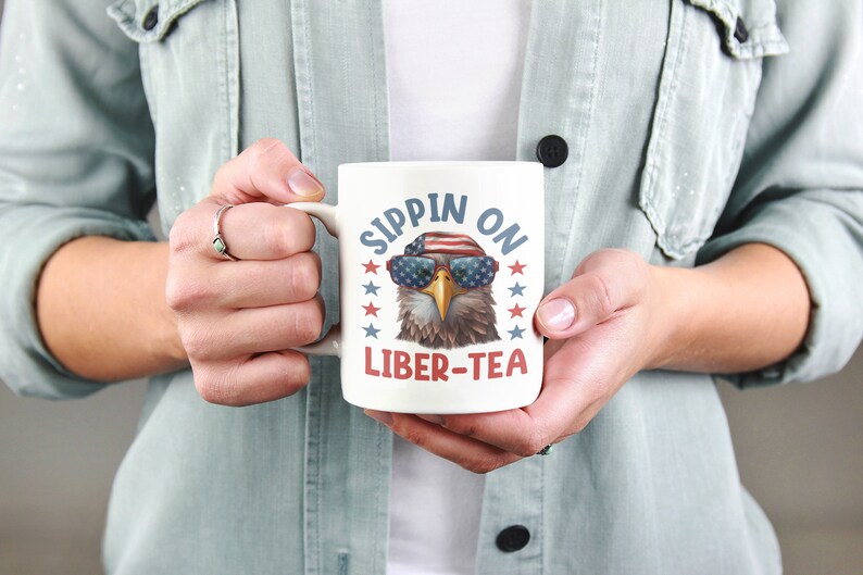 May include: White ceramic mug with a cartoon bald eagle wearing sunglasses and a red, white, and blue bandana. The text "Sippin' on Liber-Tea" is printed on the mug.