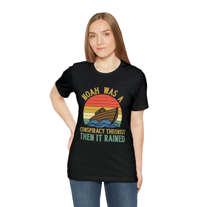 May include: A black t-shirt with a vintage-style graphic that says "Noah was a conspiracy theorist then it rained". The graphic features a rainbow and a boat.