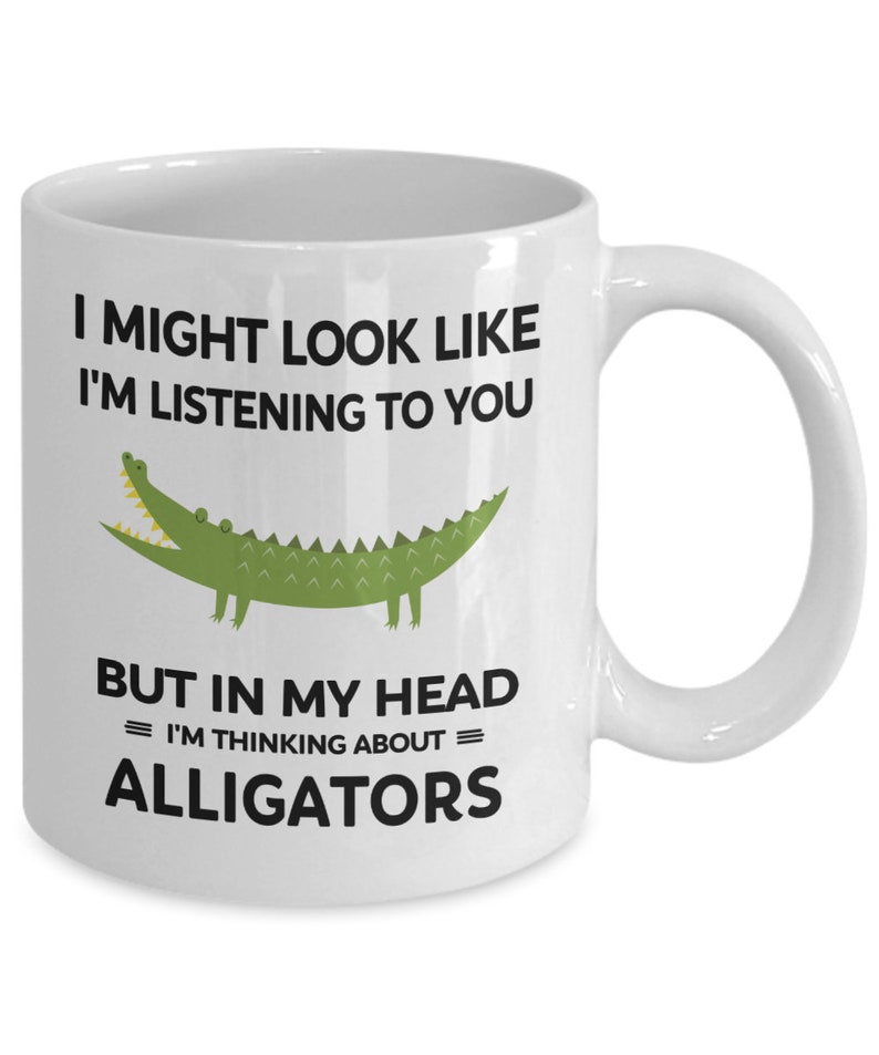 K&ouml;nnte beinhalten: Eine wei&szlig;e Keramik-Kaffeetasse mit einer gr&uuml;nen Alligator-Illustration und dem Text "I might look like I'm listening to you but in my head = I'm thinking about = alligators".
