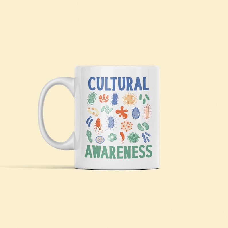 May include: White ceramic mug with a blue and green design of various bacteria and the text "CULTURAL AWARENESS".