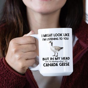 Peut inclure: Une tasse &agrave; caf&eacute; en c&eacute;ramique blanche avec une image en noir et blanc d'une oie du Canada. La tasse porte l'inscription "Je peux avoir l'air d'&eacute;couter, mais dans ma t&ecirc;te je pense aux oies du Canada."