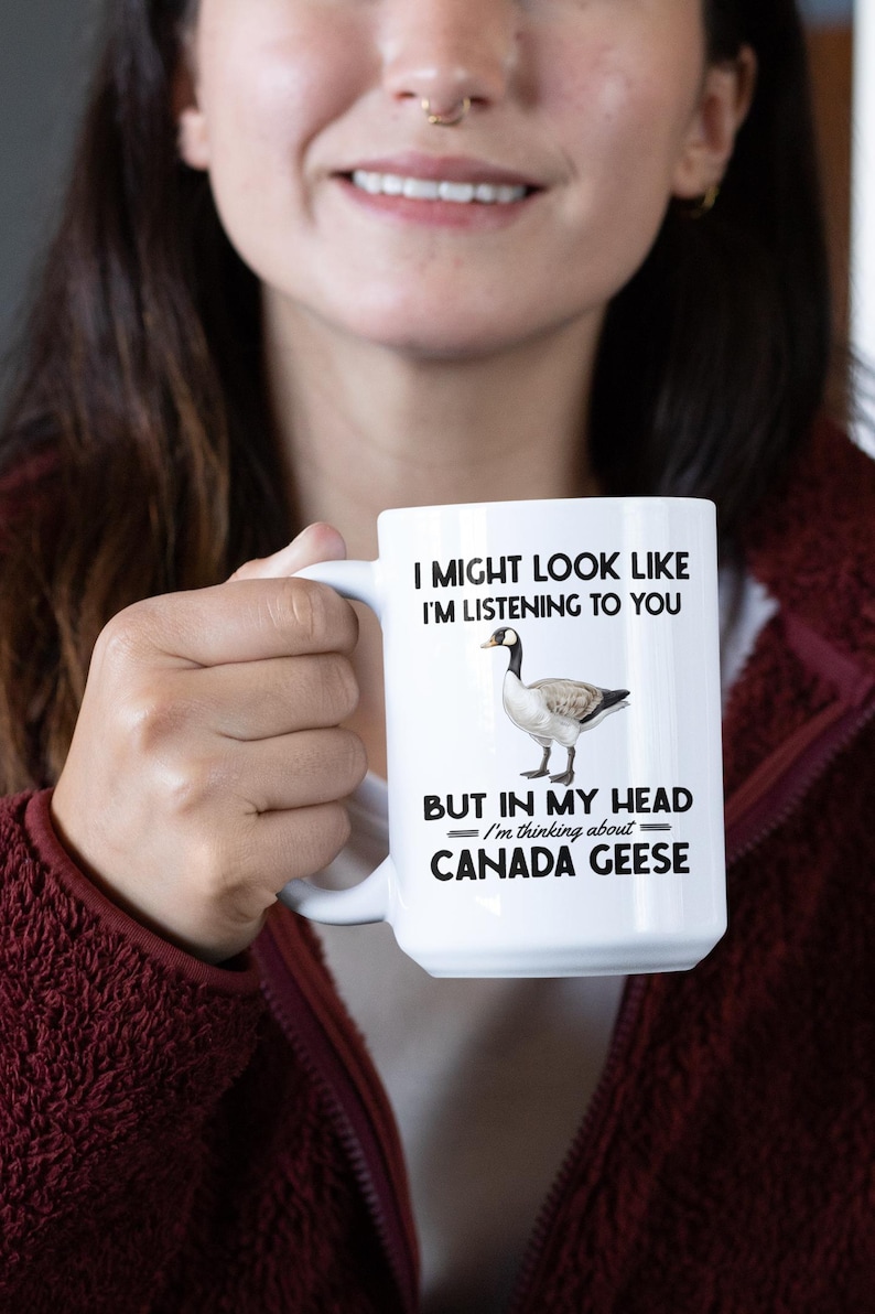 Peut inclure: Une tasse &agrave; caf&eacute; en c&eacute;ramique blanche avec une image en noir et blanc d'une oie du Canada. La tasse porte l'inscription "Je peux avoir l'air d'&eacute;couter, mais dans ma t&ecirc;te je pense aux oies du Canada."