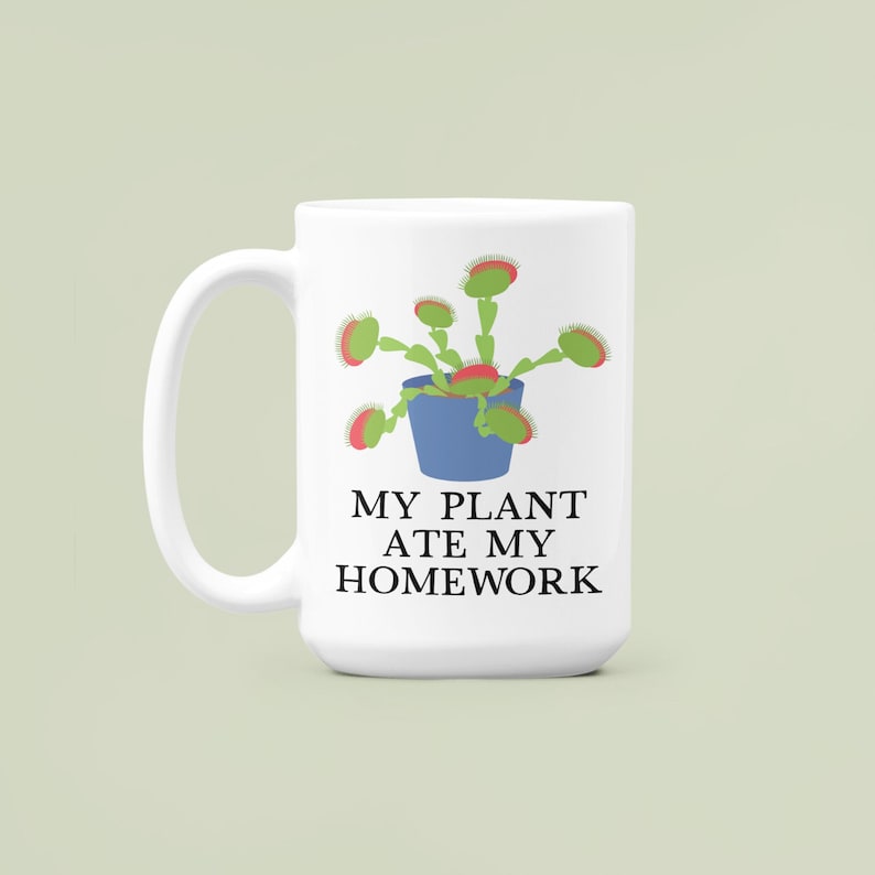 Pode incluir: Caneca de cer&acirc;mica branca com uma planta de desenho animado verde e vermelha e o texto "MY PLANT ATE MY HOMEWORK".