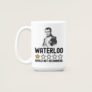 May include: White ceramic mug with a black and white image of Napoleon Bonaparte. The mug has black text that reads "WATERLOO" and a one-star rating with the text "WOULD NOT RECOMMEND."