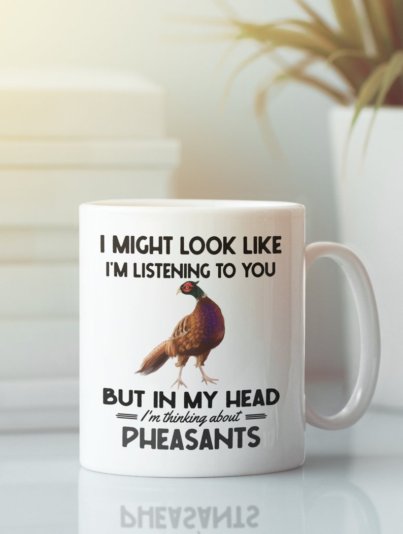 Puede incluir: Taza de caf&eacute; de cer&aacute;mica blanca con un gr&aacute;fico en blanco y negro de un fais&aacute;n. El texto en la taza dice "Puedo parecer que te estoy escuchando, pero en mi cabeza estoy pensando en faisanes."