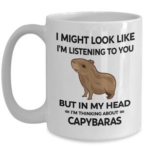 K&ouml;nnte beinhalten: Wei&szlig;e Keramik-Kaffeetasse mit einer schwarzen Grafik eines Capybaras und dem Text "Ich sehe vielleicht aus, als w&uuml;rde ich zuh&ouml;ren, aber in meinem Kopf = Denke ich an = Capybaras".