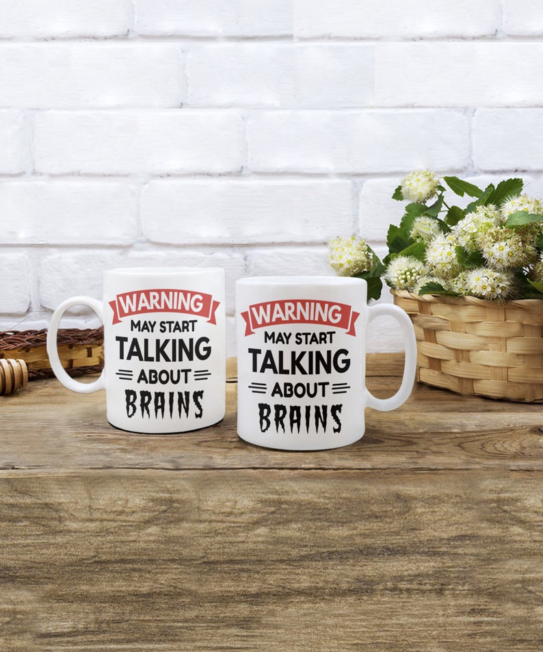 May include: Two white ceramic mugs with black text and red accents. The text on the mugs reads "WARNING MAY START TALKING = ABOUT = BRAINS".