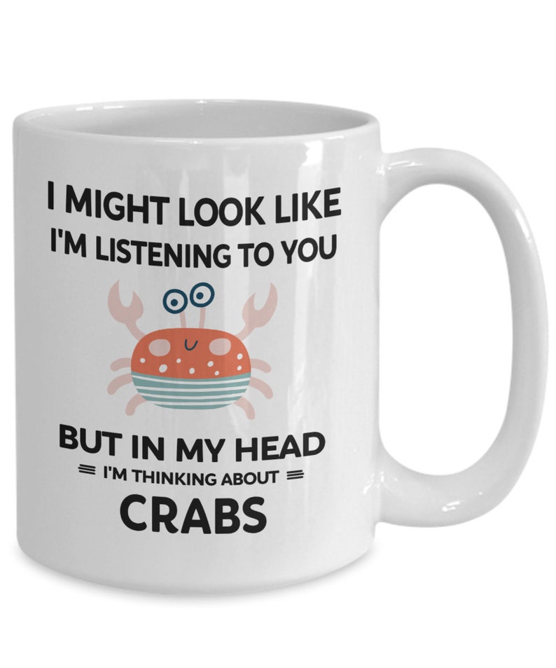 Pu&ograve; includere: Una tazza da caff&egrave; in ceramica bianca con una grafica in bianco e nero di un granchio e il testo "I might look like I'm listening to you but in my head = I'm thinking about = CRABS".