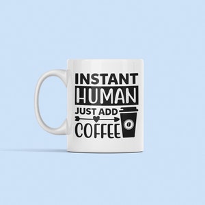 May include: White ceramic coffee mug with black text that reads "Instant Human Just Add Coffee" with a black arrow pointing to a black and white coffee cup icon.