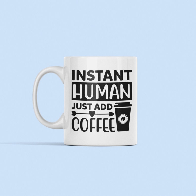May include: White ceramic coffee mug with black text that reads "Instant Human Just Add Coffee" with a black arrow pointing to a black and white coffee cup icon.
