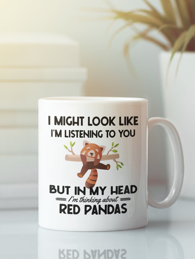 Puede incluir: Taza de cer&aacute;mica blanca con una ilustraci&oacute;n en negro y rojo de un panda rojo colgado de una rama. El texto en la taza dice "Puede que parezca que te estoy escuchando, pero en mi cabeza estoy pensando en los pandas rojos."