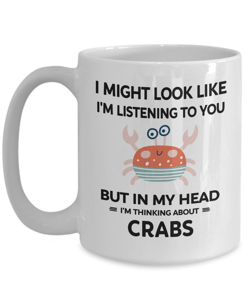 Pu&ograve; includere: Tazza da caff&egrave; in ceramica bianca con una grafica in bianco e nero di un granchio e il testo "I might look like I'm listening to you but in my head = I'm thinking about = CRABS".
