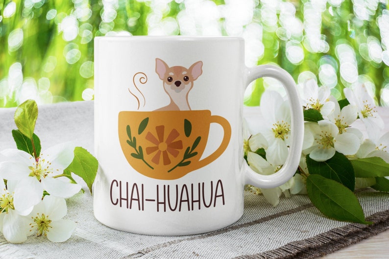 May include: White ceramic mug with a brown chihuahua dog sitting in a yellow teacup with a floral design. The text "Chai-huahua" is printed on the mug.