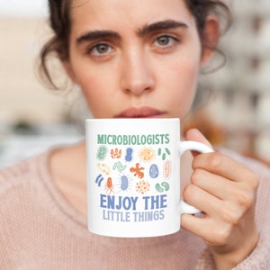 May include: White ceramic mug with a blue and green design of various microbes. The text "Microbiologists Enjoy the Little Things" is printed on the mug.